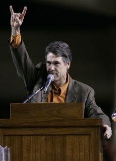 Rick Perry gives “hook em” (devil horns) at Texas university.